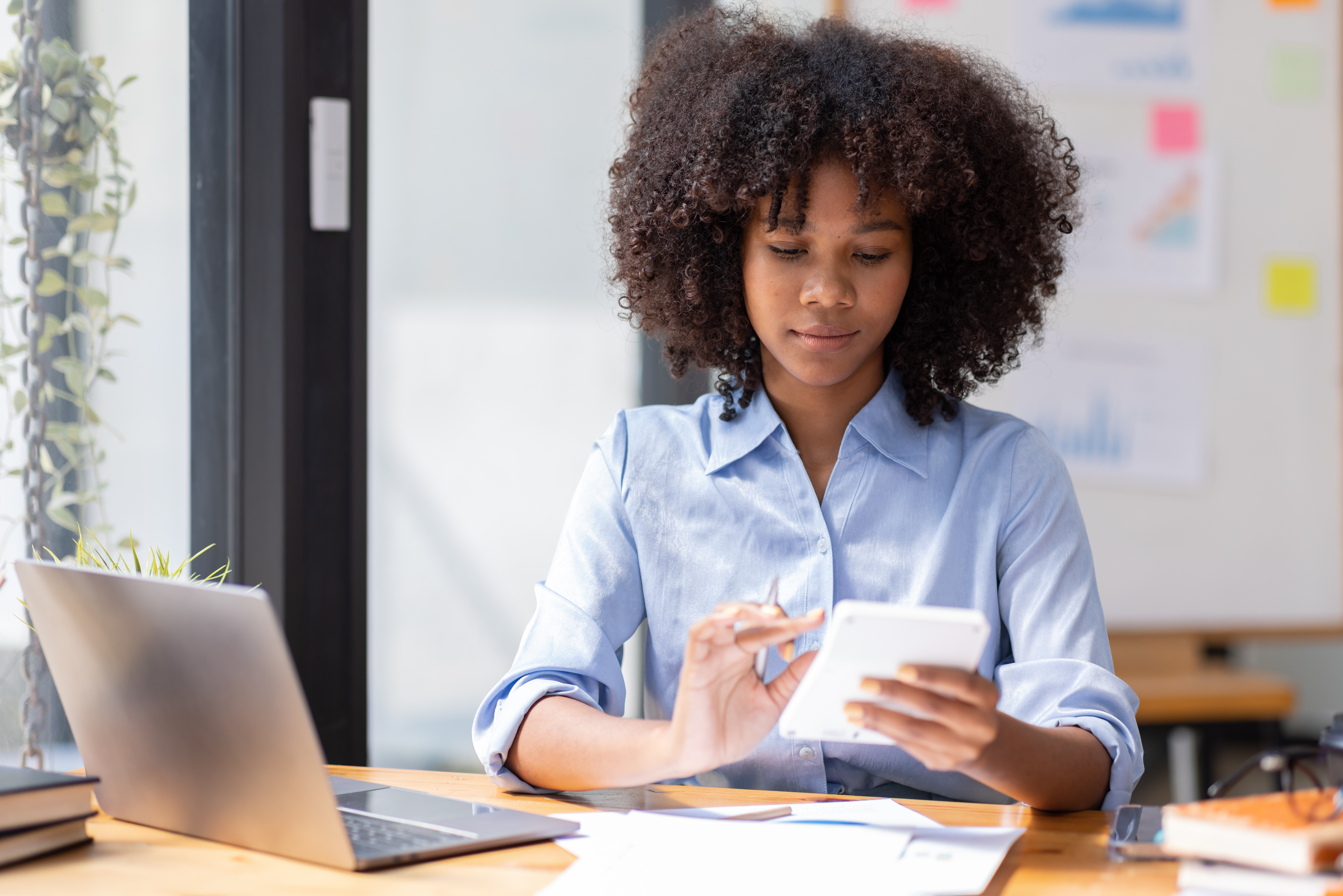 Accountant Young african businesswoman in afro hairstyle Using Calculator For documents Accounting financial sitting at computer in workplace office 
